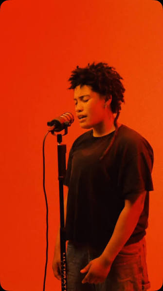 RhyRhy performing at a microphone against an orange background
